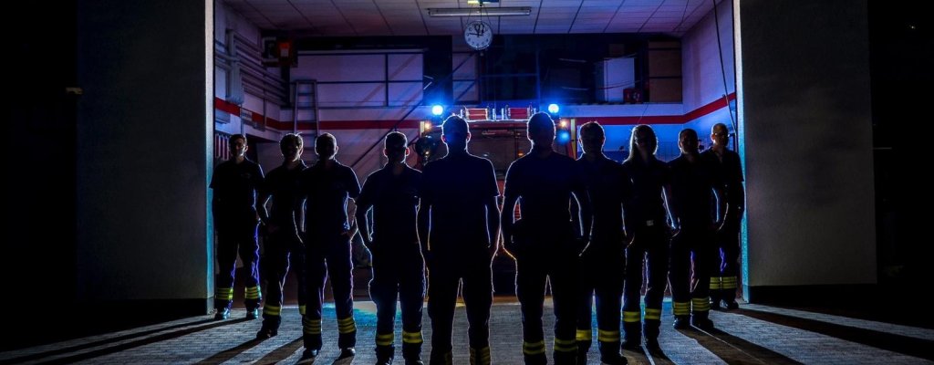 Feuerwehr im Dreieck vor dem Feuerwehrauto mit Blaulicht